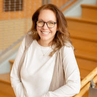 Photograph of Karen Kramer, a woman with pale skin. She is wearing an off-white long-sleeved shirt with a beige sleeveless piece over it. She has light brown hair and glasses and is looking at the camera and smiling.