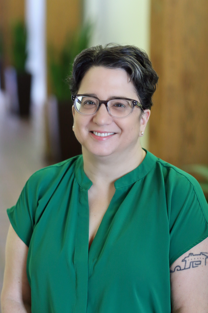 Headshot of professor Emily E LaBarbera Twarog. She's wearing a green blouse, has short dark hair and glasses, and is smiling at the camera.